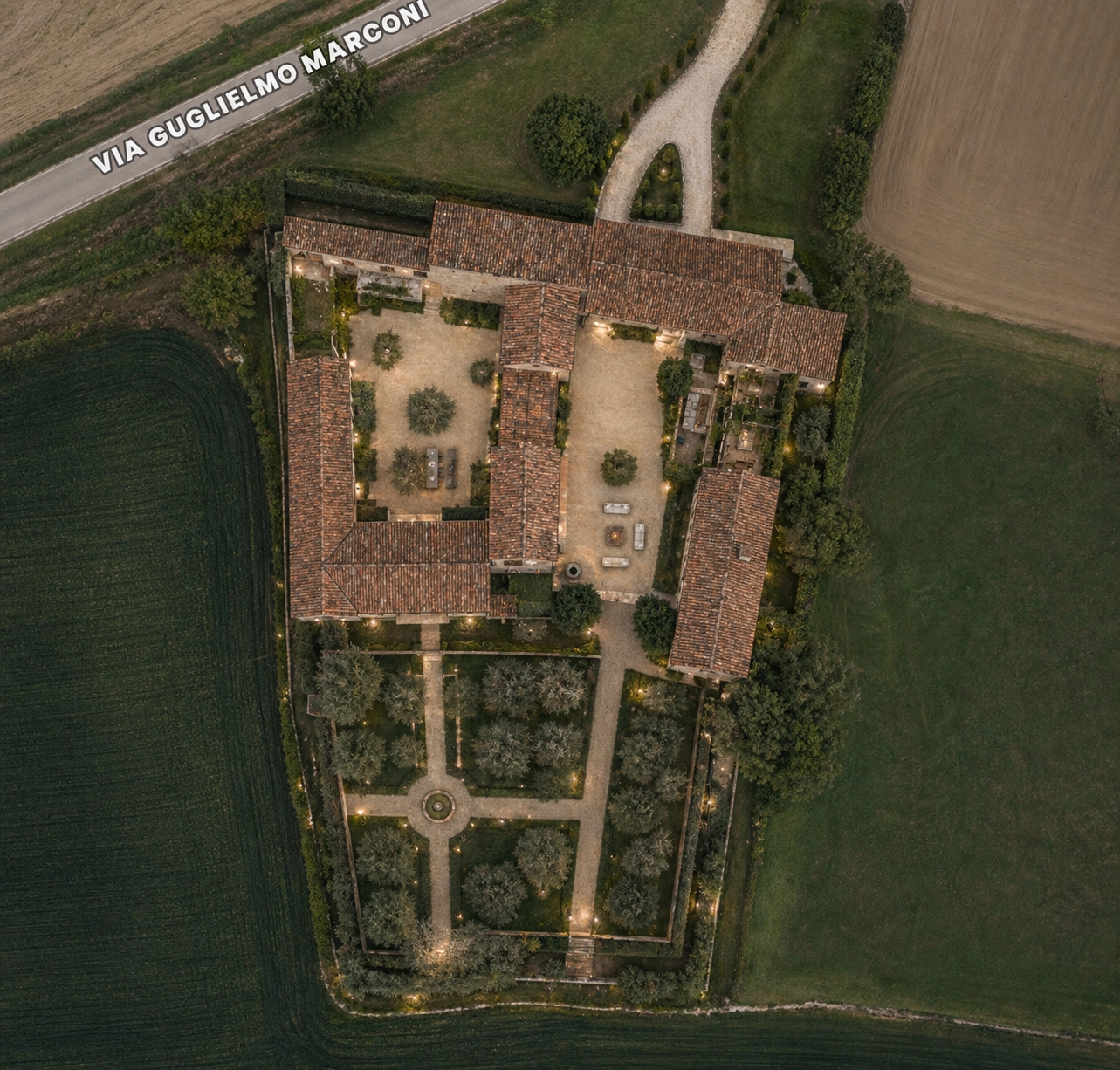 Aerial view of an illuminated Italian estate at twilight with formal gardens