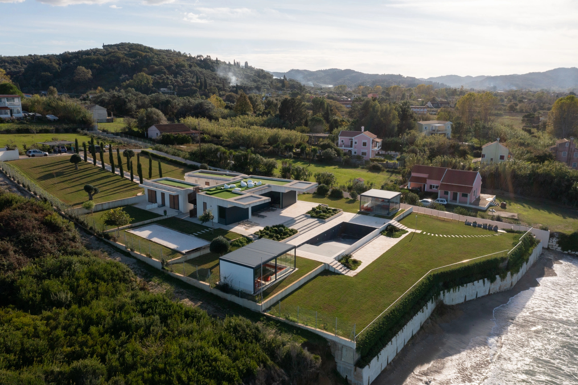 Aerial view of a modern coastal villa set within manicured gardens by the sea