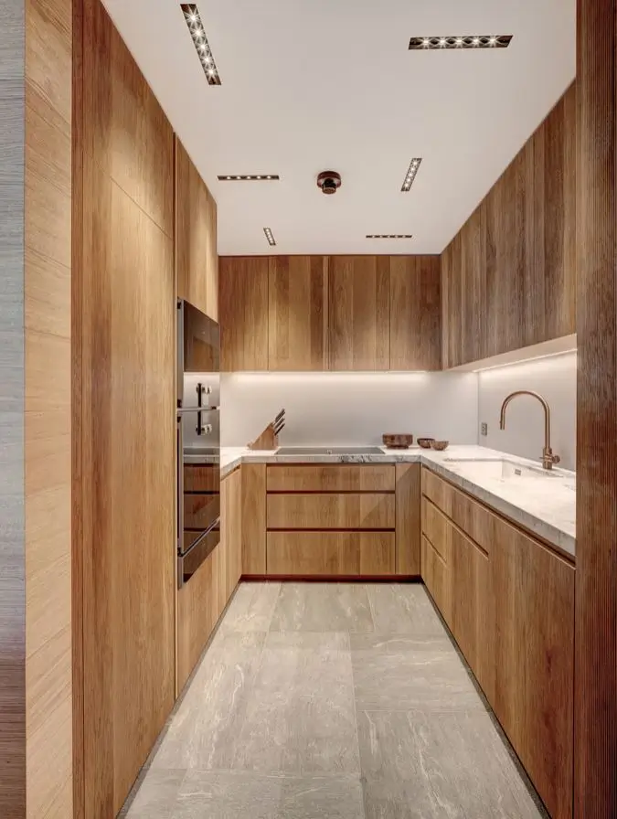 Compact galley kitchen in warm timber with marble worktops, a brass tap and an integrated oven, lit by recessed ceiling spots