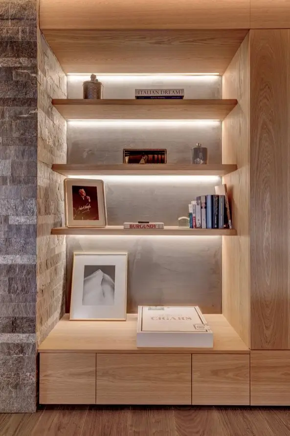 Backlit oak display shelving against a stone wall, styled with art books, framed photographs and a snow-peak picture above a low cabinet